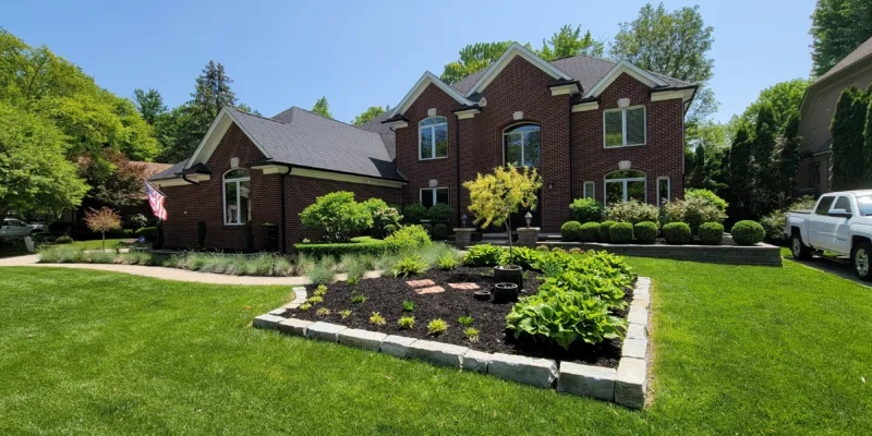A professionally designed landscape with a variety of plants, trees, and mulch in a backyard in Rochester Hills, Michigan.